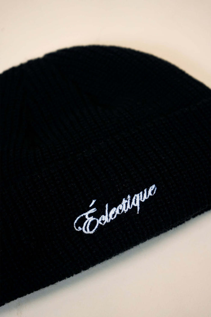 Black fisherman beanie featuring white embroidered logo 'Éclectique' on a cozy knit fabric.