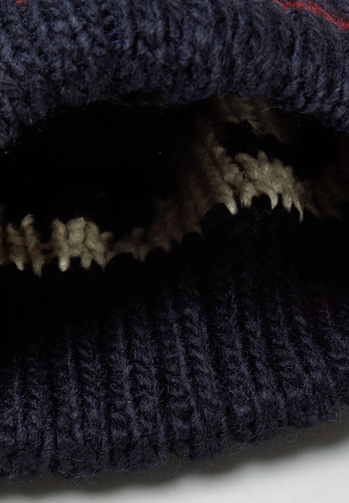 Close-up of a boys jacquard hat in navy with a pom pom and textured knit pattern.