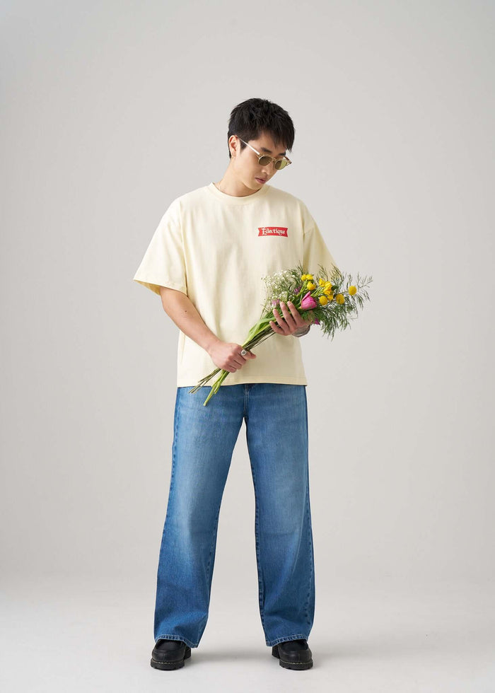 Model holding flowers wearing the Date Night Cream Graphic T-shirt by Éclectique with relaxed boxy fit and ribbed crewneck.