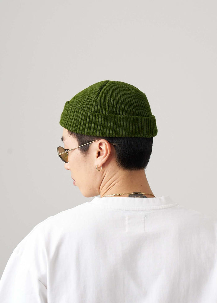 Back view of a person wearing a green fisherman beanie with sunglasses on a neutral background.