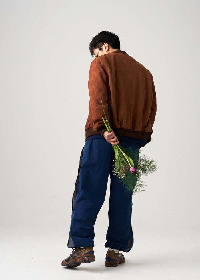 Stylish model wearing Reversible Windbreaker Pants and a brown jacket, holding flowers.
