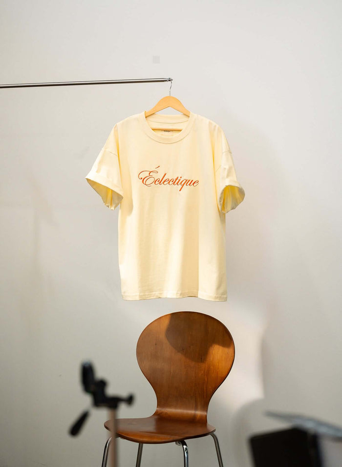 Script logo embroidered cotton t-shirt in French vanilla hanging on a rack, showcasing casual style.