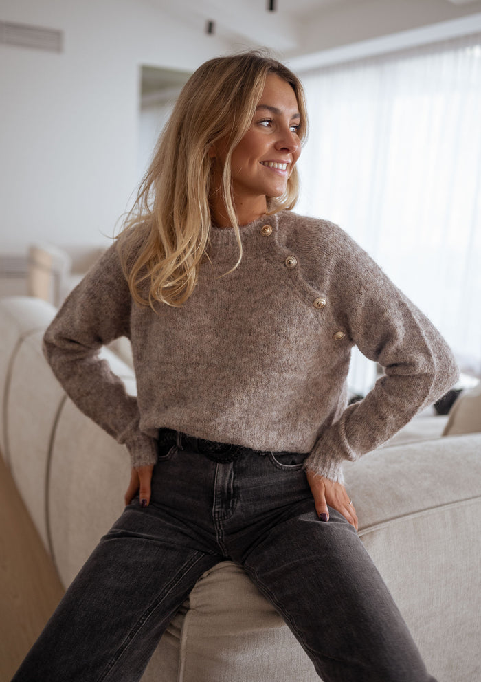 Woman wearing beige mockneck sweater with grey jeans
