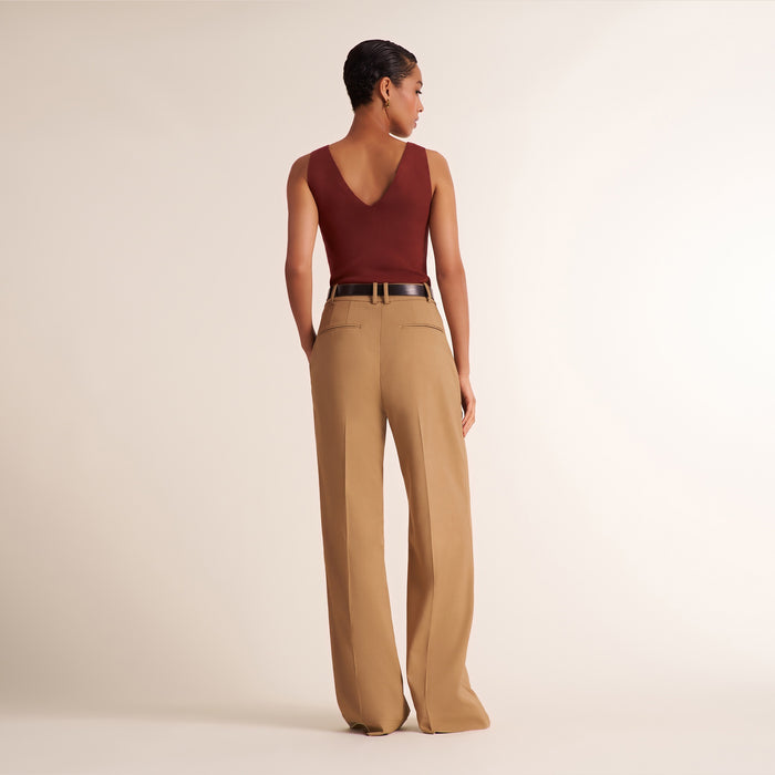 A model shown from the back wearing a sleeveless burgundy V-neck top and high-waisted tan wide-leg trousers with a thin black belt, set against a plain beige studio background.