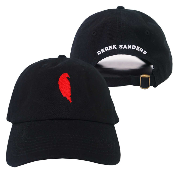Two black Derek Sanders baseball caps: one features a small red feather on the front; the other has DEREK SANDERS embroidered in white on the back above an adjustable strap with a gold buckle.
