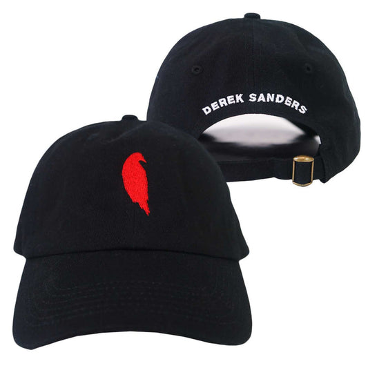Two black Derek Sanders baseball caps: one features a small red feather on the front; the other has DEREK SANDERS embroidered in white on the back above an adjustable strap with a gold buckle.