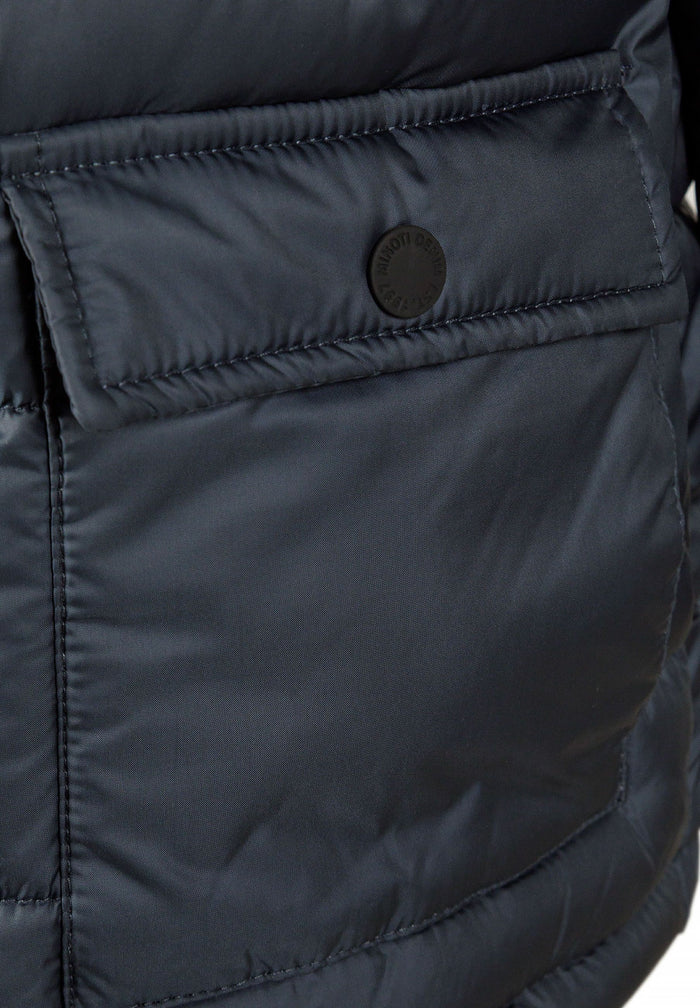 Detail of a navy boys jacket with a rubber badge and flap pocket.