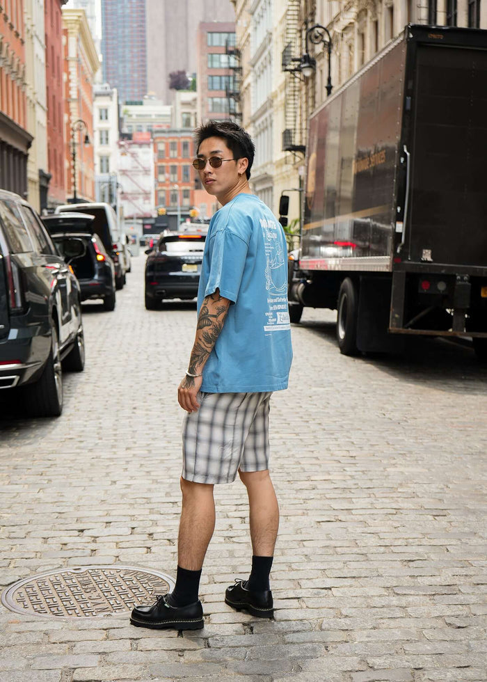 Man wearing Carolina Blue Date Night T-shirt with plaid shorts in a trendy urban street setting.
