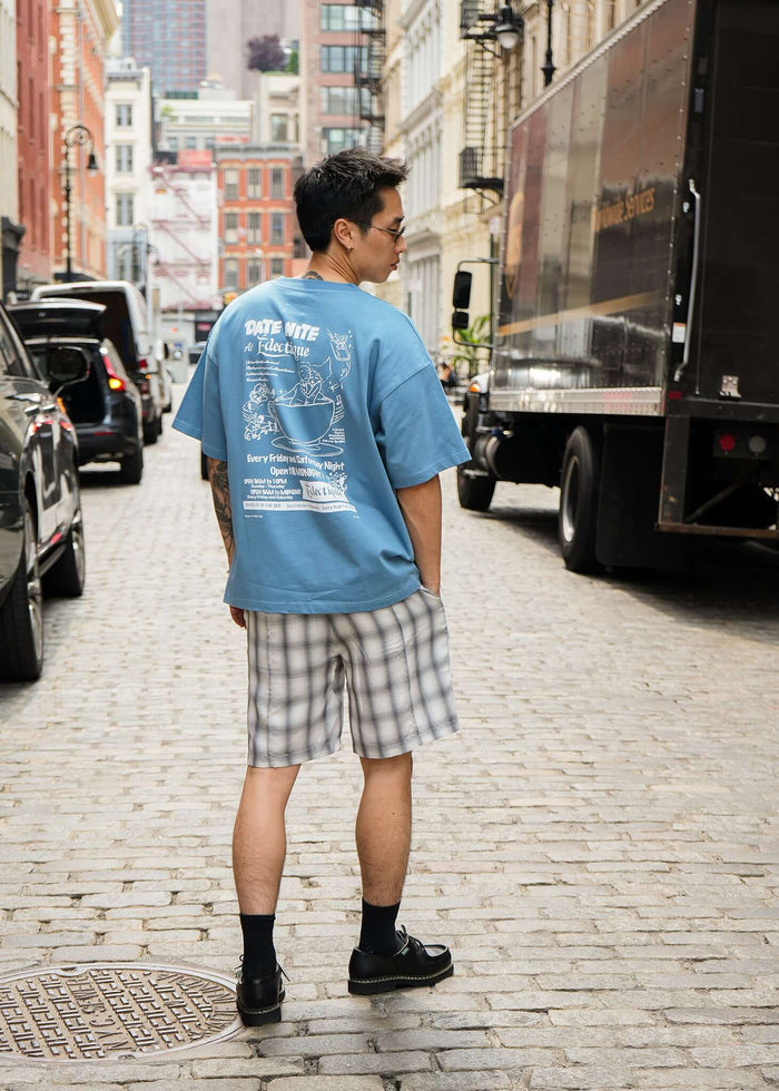 Man wearing Carolina Blue Date Night T-shirt with plaid shorts, standing on a city street.