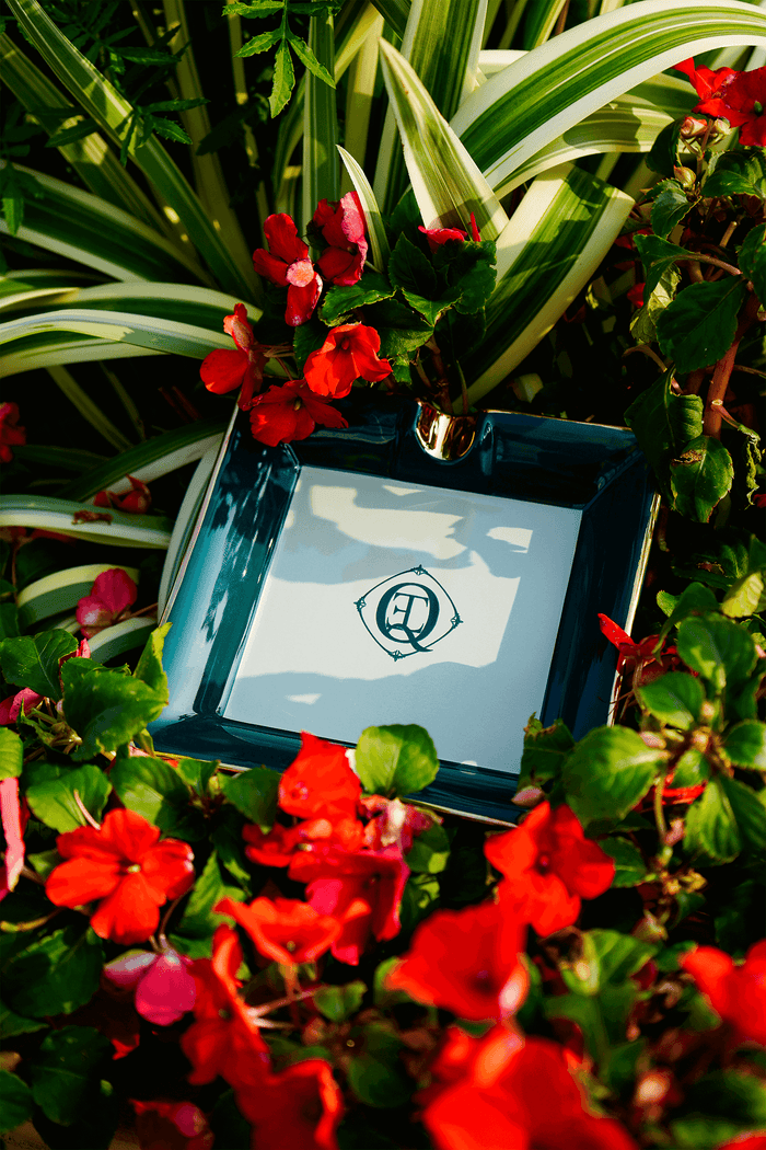 Monogram gold trim ceramic catchall tray surrounded by vibrant flowers in a garden setting.