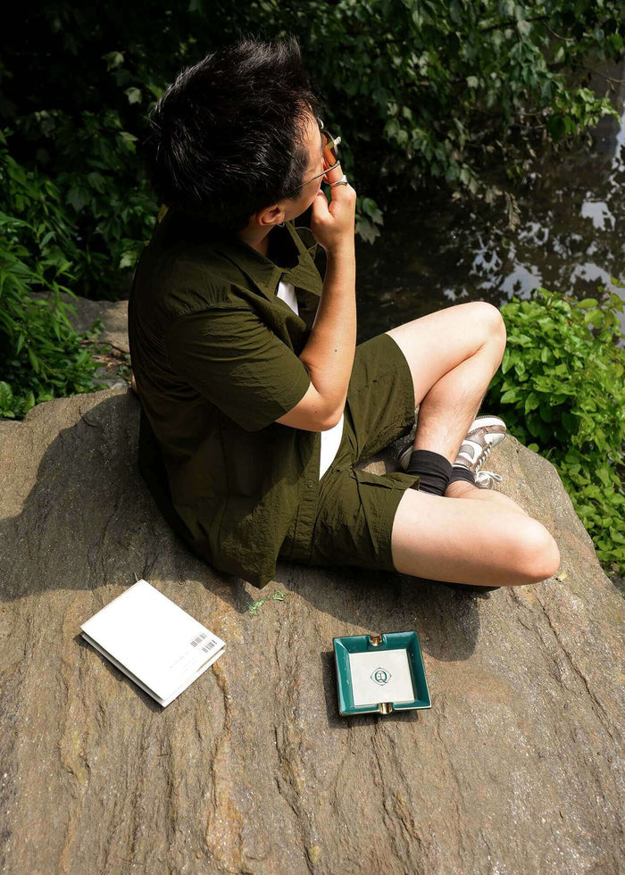 A person sitting on a rock by the water, with a ceramic catchall tray nearby, showing its elegant design.