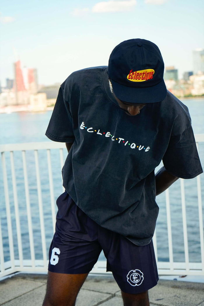 Model wearing Eclectique classic Friends logo t-shirt and cap by the waterfront with a city skyline in the background