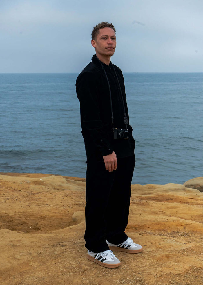 Model wearing a Corduroy Button-Up Shirt by Mercer near the ocean, showcasing a stylish outdoor look.