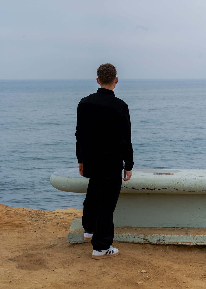 Man facing the ocean wearing a black Corduroy Button-Up Shirt on a coastal cliff.