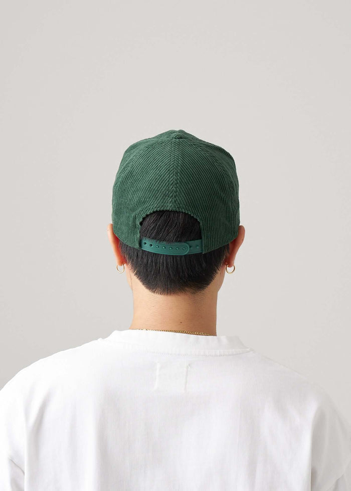 Person wearing a Corduroy script logo snapback hat in June Bug Green, showing adjustable snapback closure from the back.