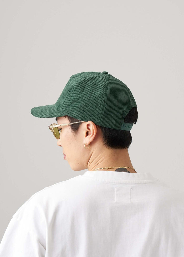 Corduroy script logo snapback hat worn by person from the back, featuring June Bug Green color and adjustable snapback.