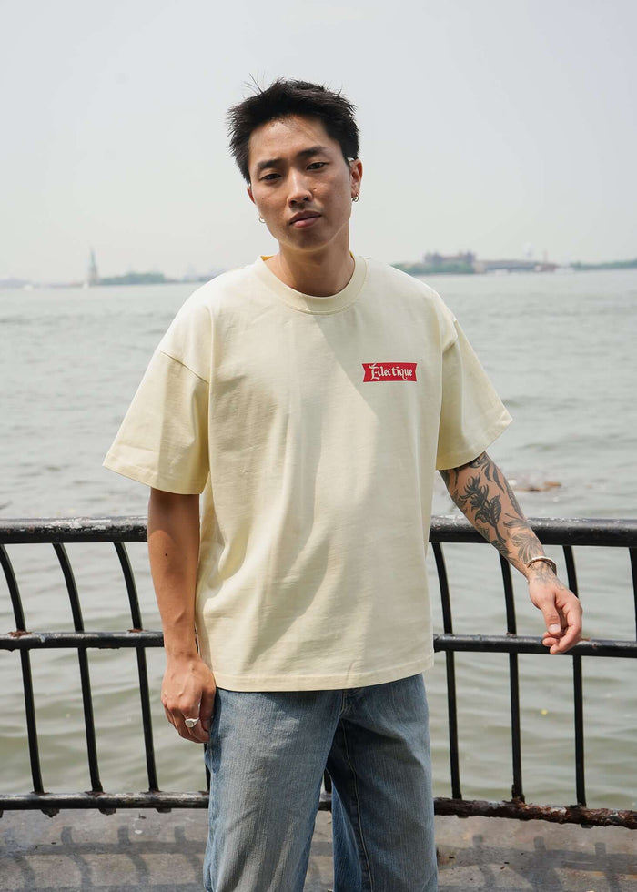 Model wearing a relaxed fit cream graphic T-shirt by Éclectique with Date Night artwork, standing by the water.