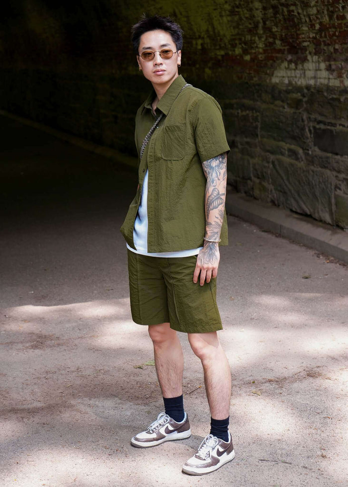 Man wearing a stylish olive designer short sleeve casual shirt paired with shorts in an outdoor setting.