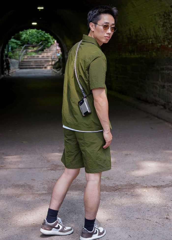 Man wearing a designer short sleeve casual shirt in olive green, styled with shorts and sneakers.