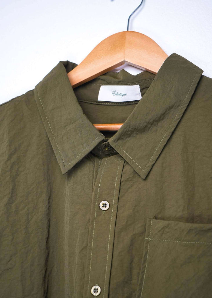 Close-up of a designer short sleeve casual shirt in olive green hanging on a wooden hanger.