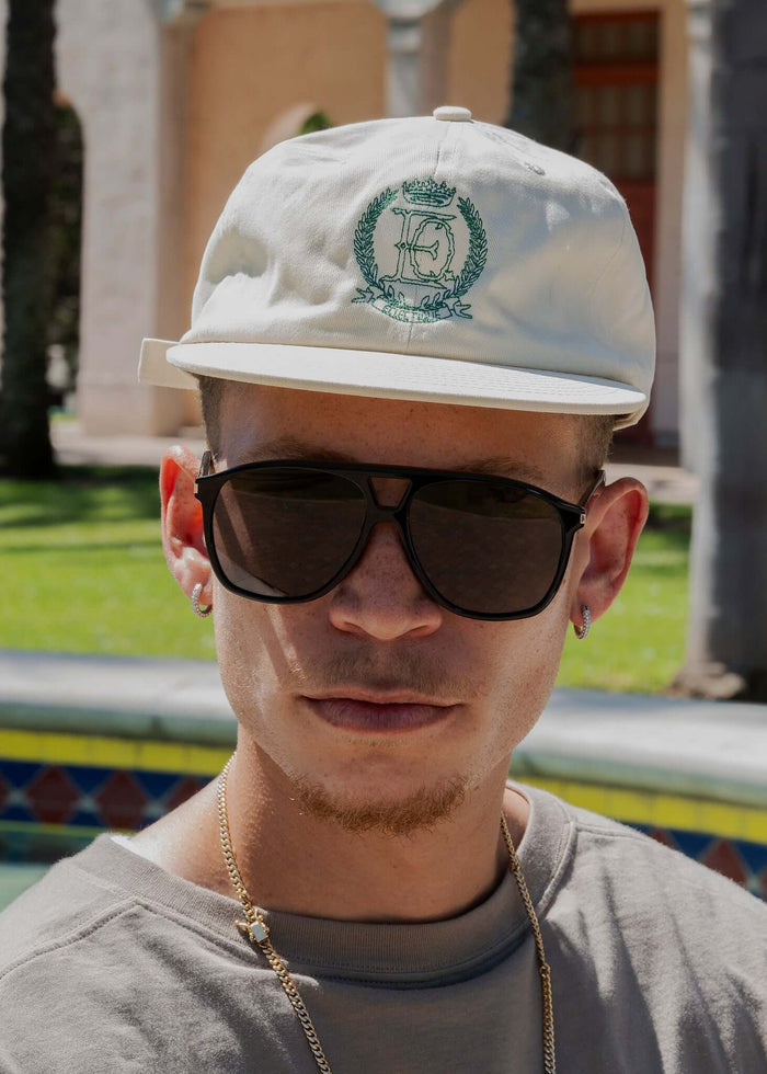Man wearing Éclectique Crest embroidered dad hat with sunglasses in outdoor setting.
