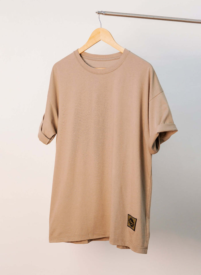 Japanese Made Essential Cotton T-shirt in sand color hanging on a rack with a woven label at the hem.