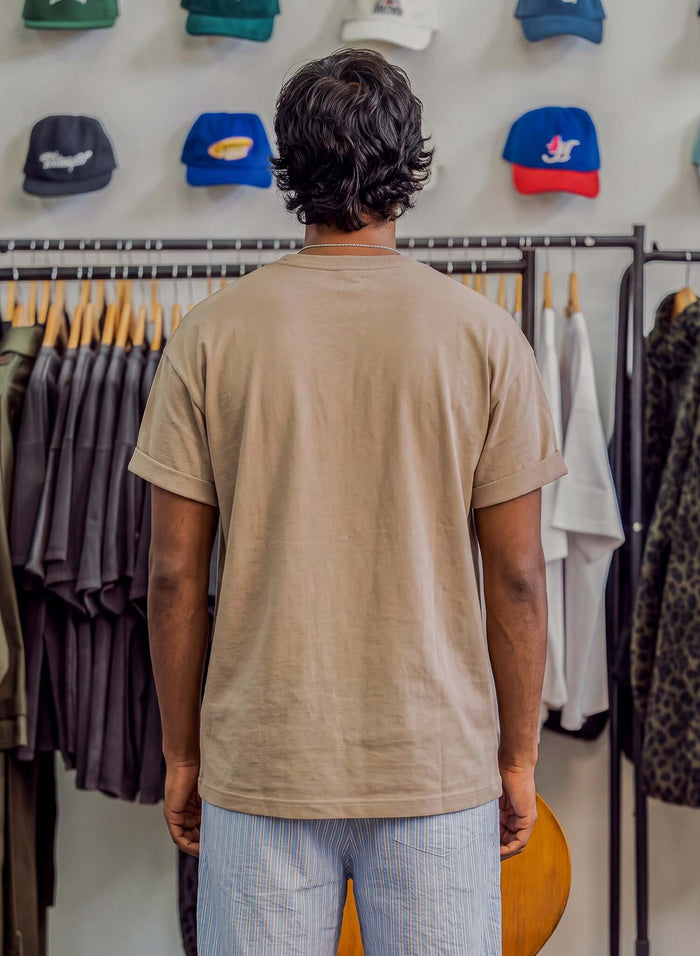 Man wearing the Essential Cotton T-shirt in sand, viewed from the back, showcasing its relaxed fit.