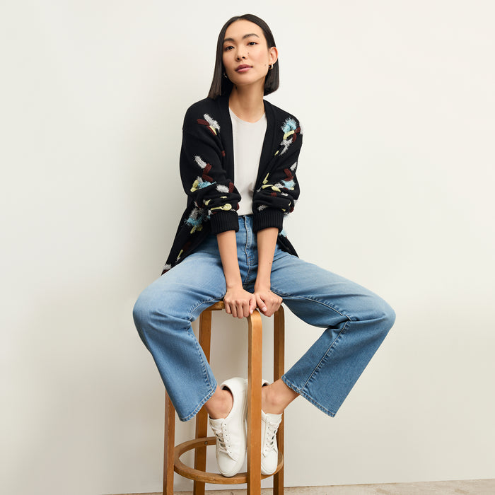 front image of a woman sitting wearing the frame le jane ankle jeans in deepwater