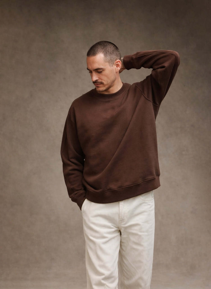 Model wearing a brown French Terry crewneck sweatshirt with white pants, showcasing style and comfort.