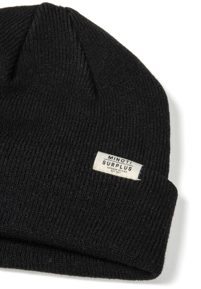 Detail of a black ribbed beanie hat with a fold-up cuff and a small logo badge.