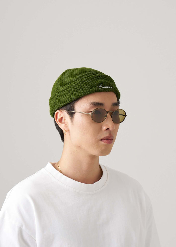 Man wearing a green fisherman beanie with white logo embroidery and sunglasses.