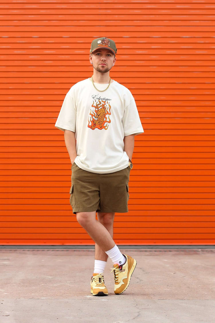 Model wearing a Jaguar Graphic T-shirt with flaming jaguar design and khaki shorts against an orange background.