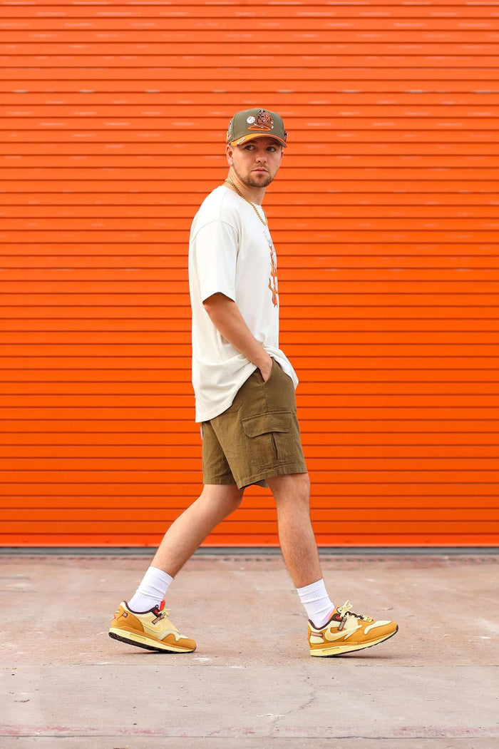 Man wearing a Jaguar Graphic T-shirt with cargo shorts and sneakers, standing against an orange backdrop.