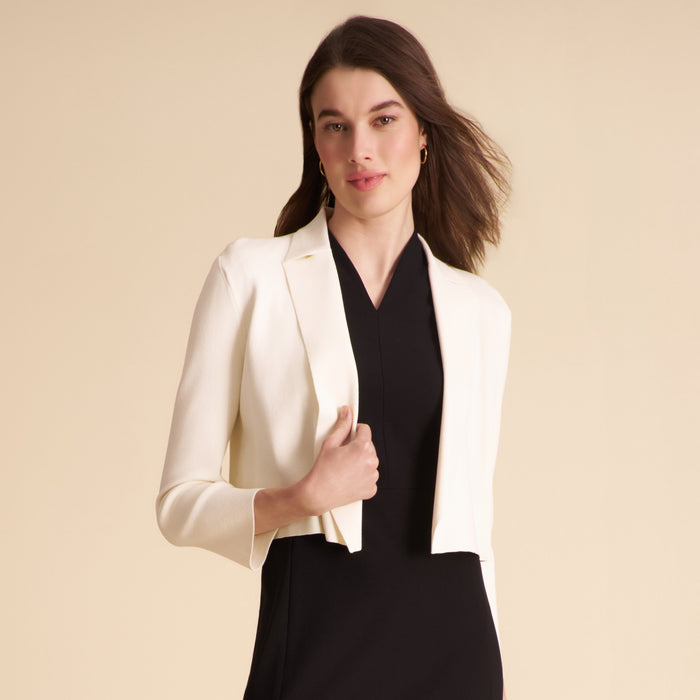 Woman wearing a white blazer over a black dress on a beige background | Lead