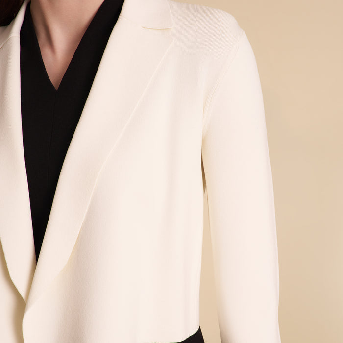 Woman wearing a white blazer over a black dress on a beige background