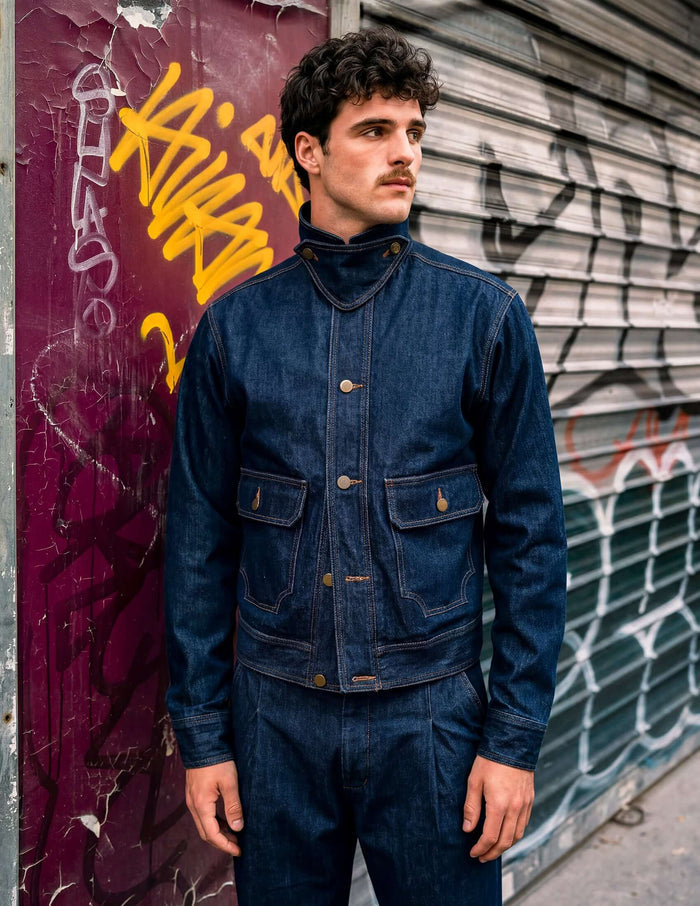 Kura Indigo Jacket modeled against a graffiti background, showcasing its deep indigo color and unique design features.