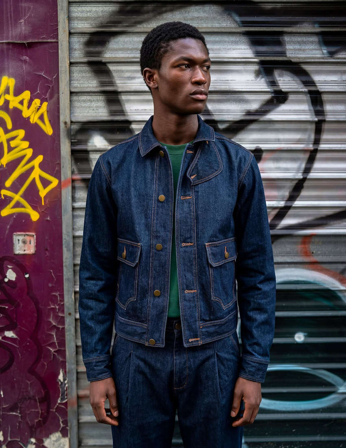 Model wearing the Kura Indigo Jacket styled with urban graffiti background, showcasing its deep indigo wash and unique details.