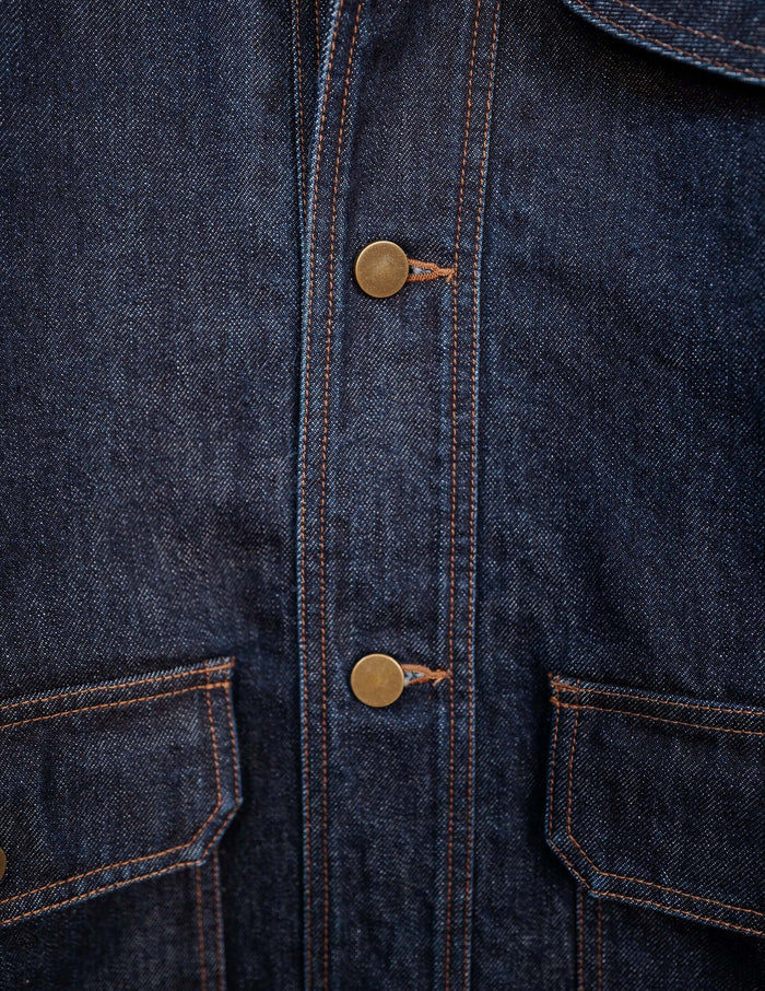 Close-up of Kura Indigo Jacket showing deep indigo fabric, brass buttons, and flap pockets detail.
