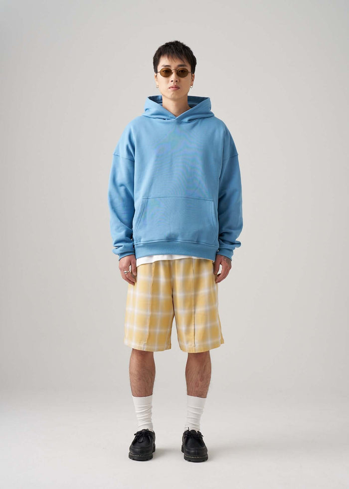 Model wearing a lightweight terry hoodie in blue with yellow plaid shorts and sunglasses.