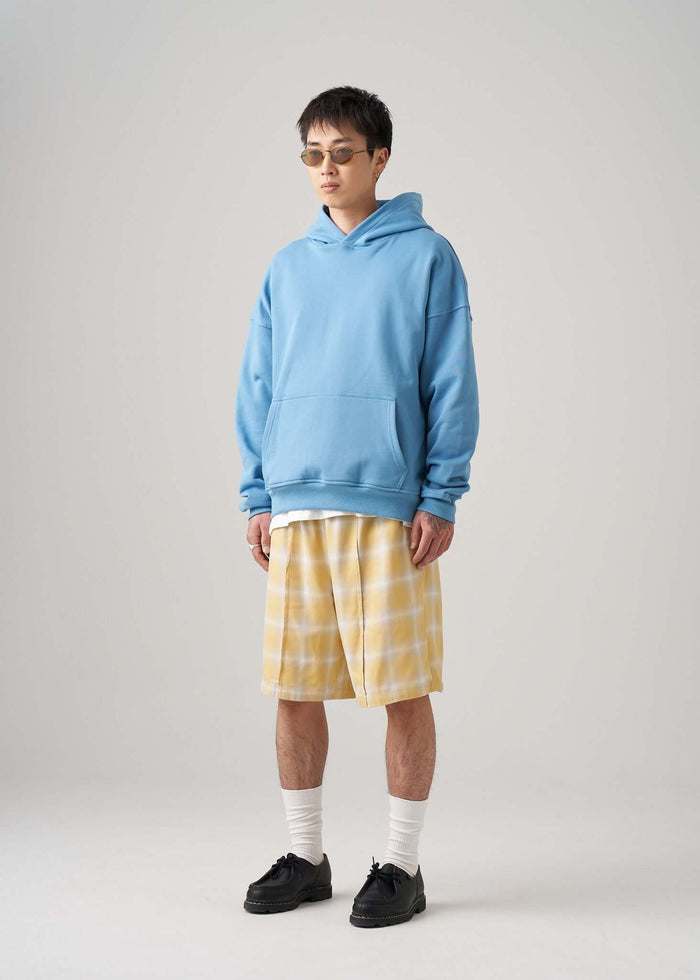 A model wearing a lightweight terry hoodie in cotton jersey with yellow plaid shorts and sunglasses.