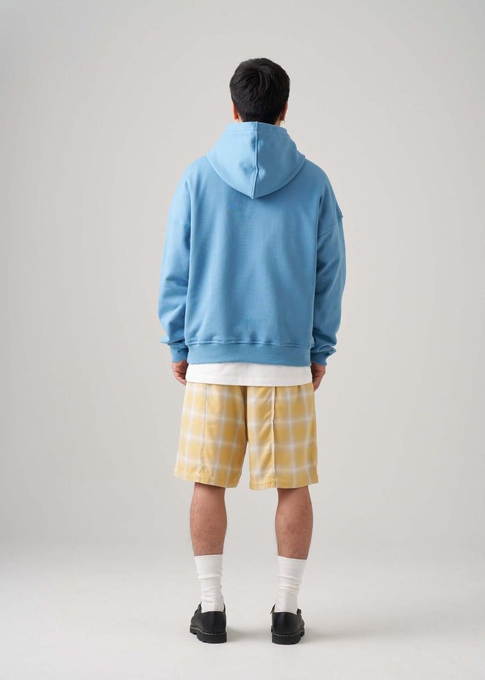 A man wearing a lightweight terry hoodie in blue, paired with yellow plaid shorts, showcasing a casual back view.
