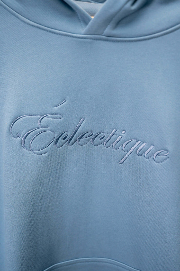 Close-up of Lightweight Terry Hoodie with Script Logo from Éclectique, showcasing soft fabric and embroidered logo detail.
