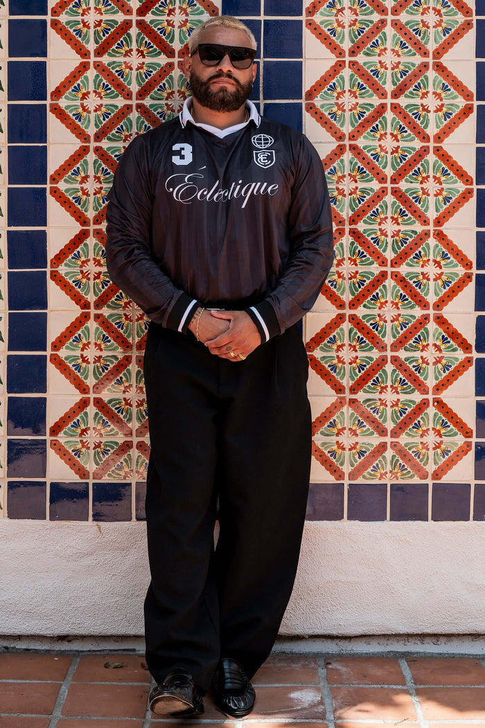 Stylish man in Long Sleeve Soccer Jersey posing against colorful tiled wall.