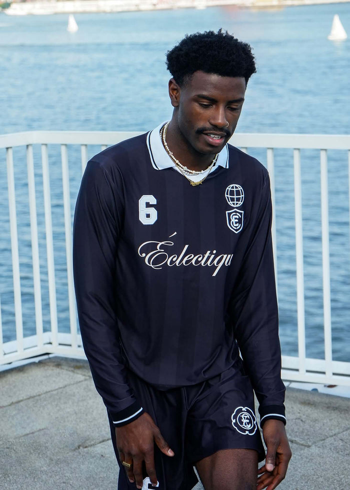 Long Sleeve Soccer Jersey worn by a model by the water, featuring a black design and embroidered details.