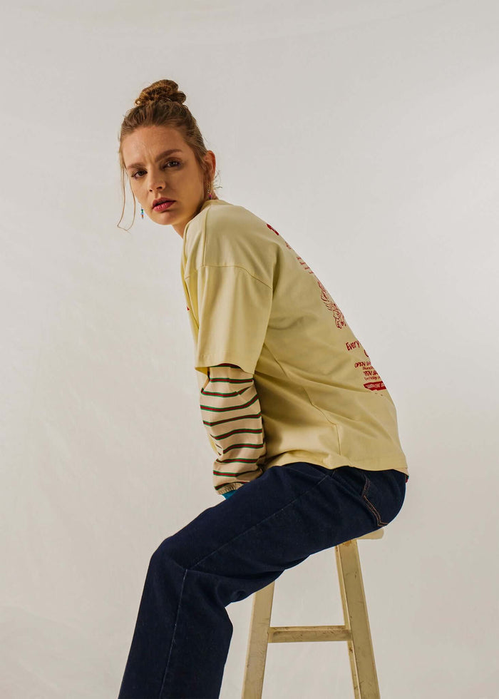 Model wearing a Twofold Drift Long Sleeve T-shirt with stripes, sitting on a stool, showcasing a relaxed style.