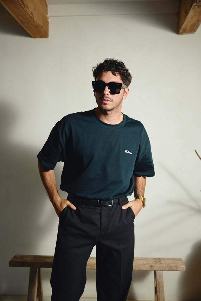 Men's oversized embroidered t-shirt styled with dark pants and sunglasses, showcasing a relaxed fashion look.