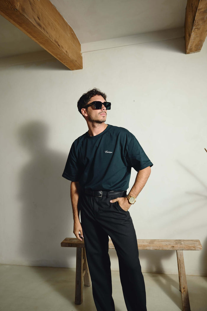 Men's oversized embroidered t-shirt worn by a man in sunglasses, styled with black pants and a relaxed pose.