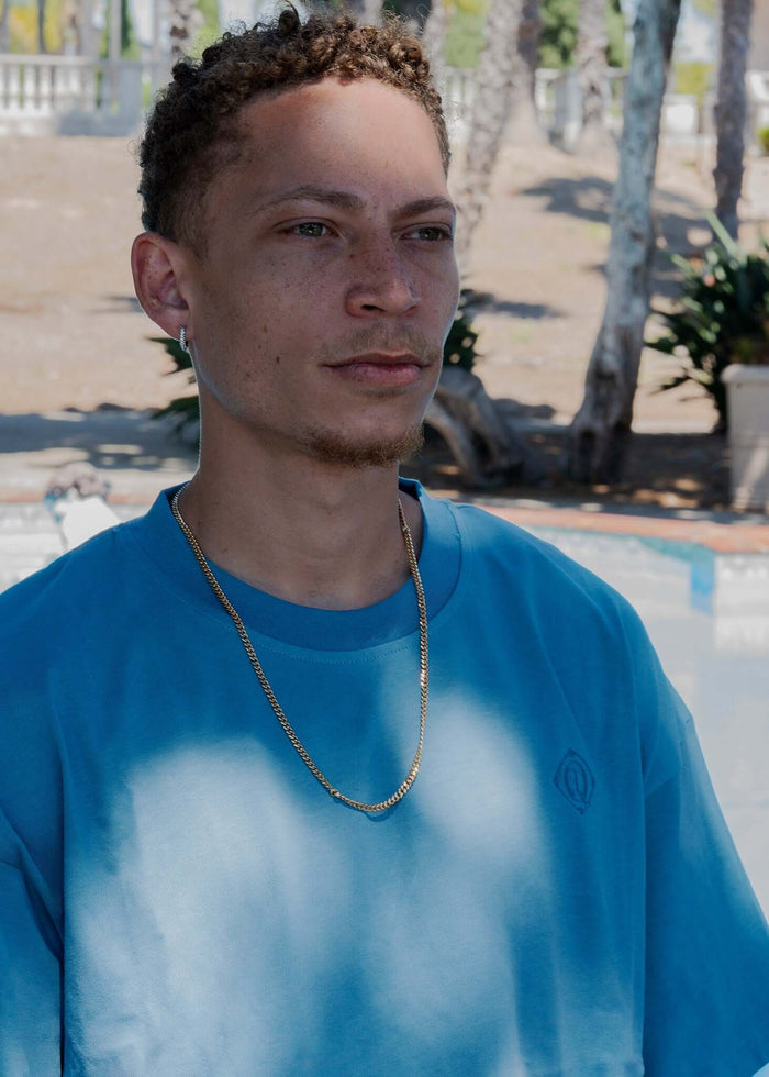 Monogram embroidered cotton t-shirt in blue worn by a man outdoors, showcasing the embroidered logo and casual style.