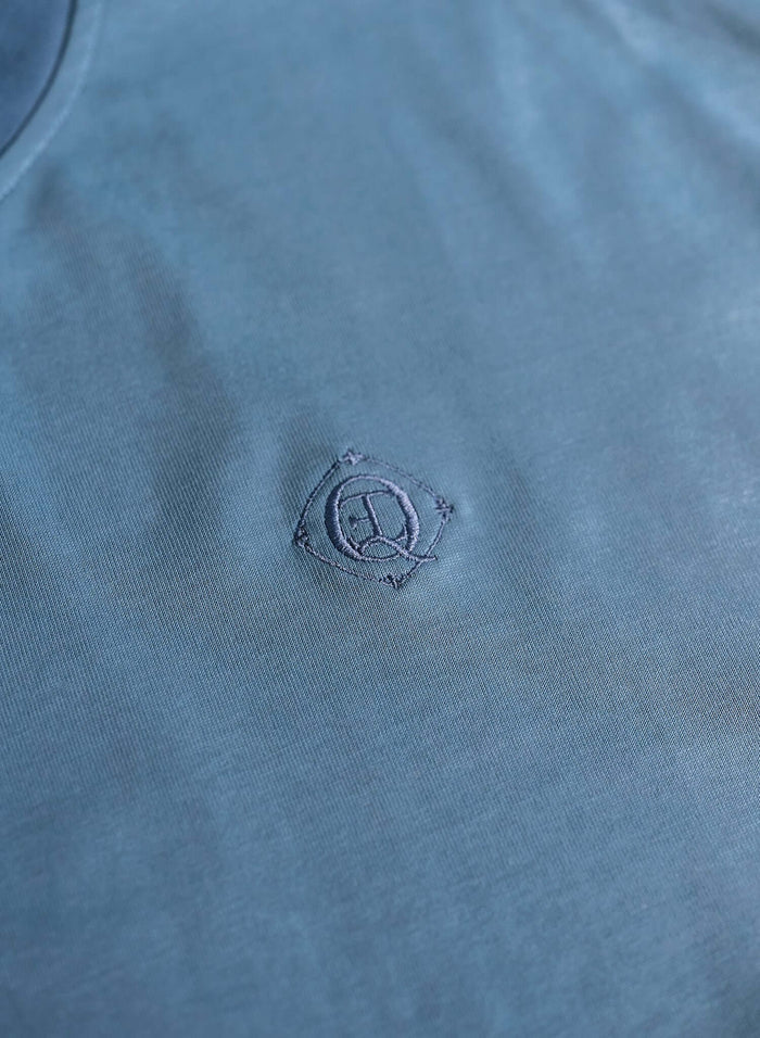 Monogram embroidered cotton t-shirt close-up showing embroidered monogram logo on blue fabric.