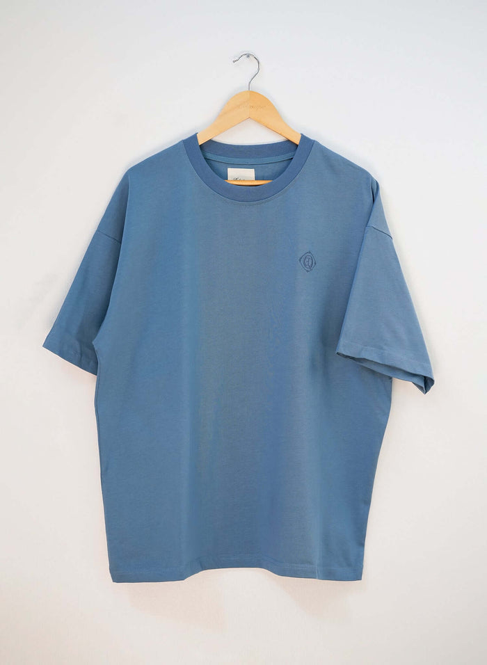 Monogram embroidered cotton t-shirt in blue hanging on a wooden hanger showcasing its clean silhouette.